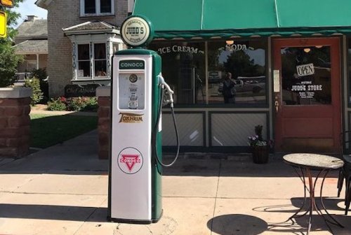 A vintage Conoco gas pump stands outside a charming ice cream shop with a green awning and open sign.