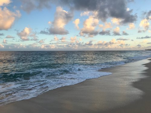 A serene beach scene with gentle waves lapping at the shore under a sky filled with fluffy clouds.