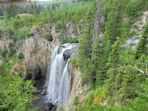 A scenic waterfall cascading down rocky cliffs, surrounded by lush green trees and a serene landscape.
