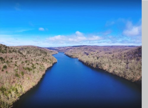 Aerial view of a serene river winding through wooded hills under a clear blue sky.