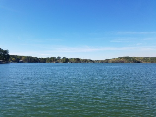 A serene lake surrounded by green hills under a clear blue sky.