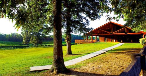 A rustic wooden pavilion surrounded by lush green fields and trees, with a pathway leading to it.