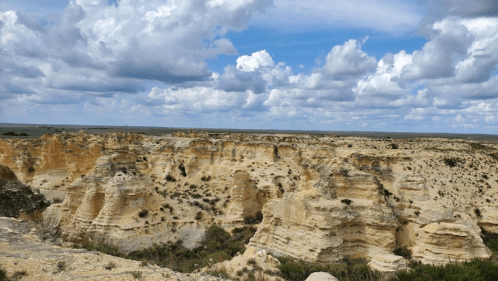 A panoramic view of rugged cliffs and rock formations under a cloudy blue sky.