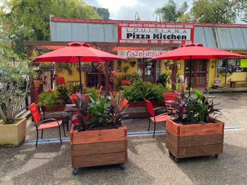Outdoor dining area with red umbrellas, potted plants, and chairs in front of Louisiana Pizza Kitchen.