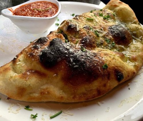 A golden-brown stuffed naan with charred spots, served with a small bowl of red dipping sauce.