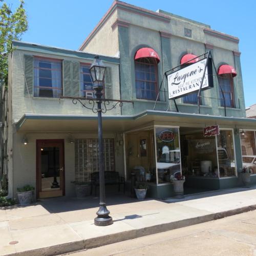 A charming restaurant with a sign reading "Loyanne's" and green awnings, set in a quaint, sunny street.