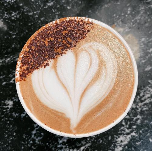 A top view of a latte with a heart-shaped foam design, sprinkled with cocoa powder on one side.