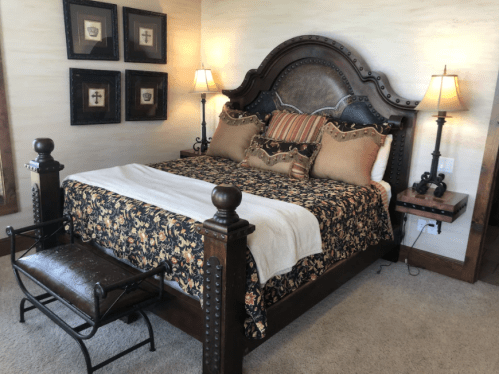 A cozy bedroom featuring a large wooden bed with decorative pillows, a patterned bedspread, and bedside lamps.