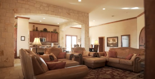 Spacious living room with leather sofas, warm lighting, and a view of a kitchen area in a cozy home.