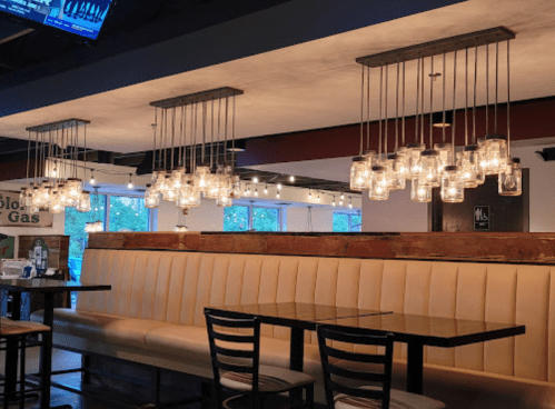 A cozy restaurant interior featuring hanging jar lights, a beige booth, and dark tables.