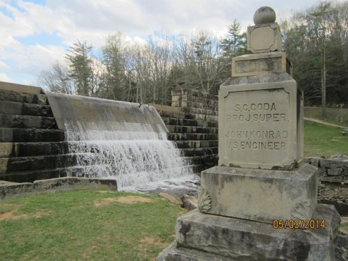 A stone monument beside a waterfall, with trees and cloudy skies in the background.