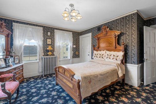 A vintage bedroom with a wooden bed, floral wallpaper, a mirror, and a radiator, featuring a cozy, classic design.