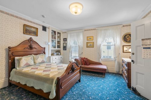 Cozy bedroom with a wooden bed, patterned quilt, vintage decor, and a chaise lounge by the window.