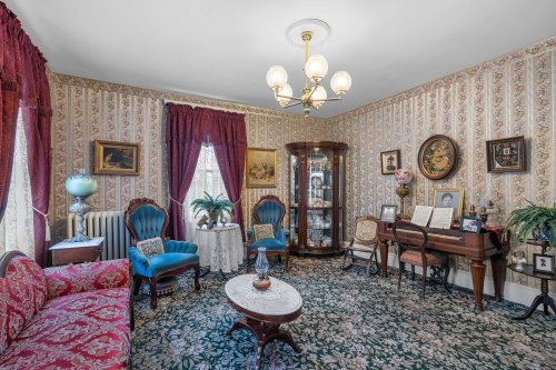 A vintage living room with floral wallpaper, a piano, elegant furniture, and decorative plants.