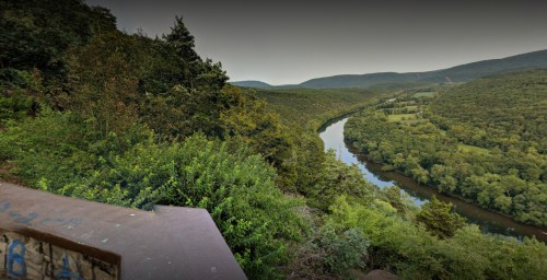 A scenic view of a winding river surrounded by lush green hills and trees under a cloudy sky.