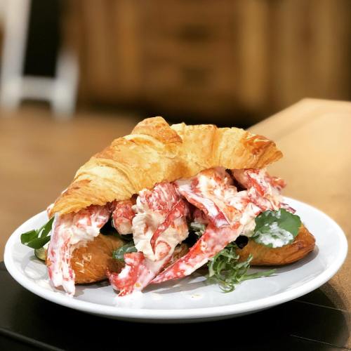 A croissant sandwich filled with lobster, greens, and creamy sauce, served on a white plate.