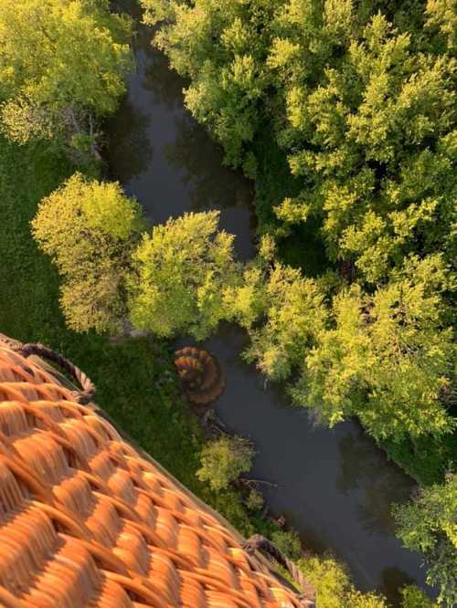 Aerial view of a lush green landscape with a winding stream and a hot air balloon partially visible below.