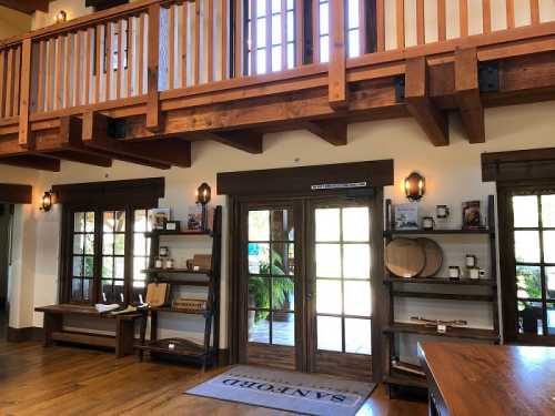 Interior of a rustic space featuring wooden beams, shelves with items, and large glass doors leading outside.