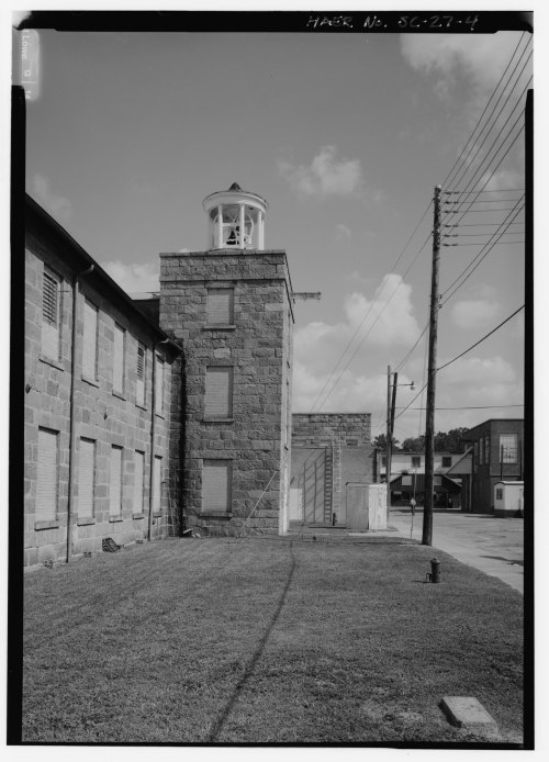 Historic stone building with a tower, surrounded by grass and power lines, under a clear sky.