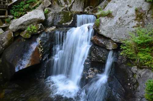 A serene waterfall cascading over rocks, surrounded by lush greenery and natural stone formations.