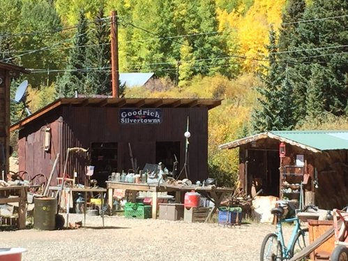 A rustic building labeled "Goodrich Silvertown" surrounded by trees with autumn foliage and various outdoor items.