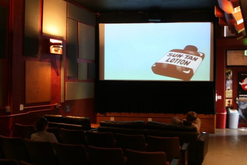A nearly empty movie theater with a screen displaying a sun tan lotion bottle.