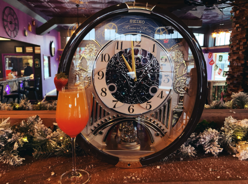 A decorative clock with a cocktail in front, set in a vibrant, festive bar environment.