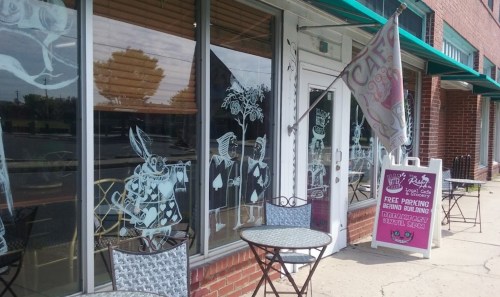 A café entrance with decorative window art, outdoor seating, and a sign for free parking nearby.