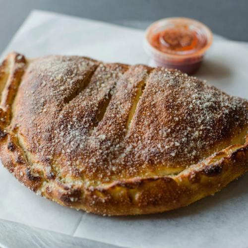 A golden-brown calzone with a crispy crust, served with a small cup of marinara sauce on the side.