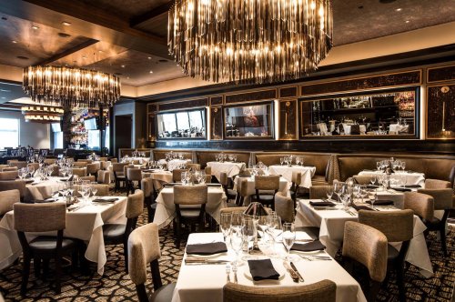 Elegant restaurant interior with tables set for dining, featuring chandeliers and stylish decor.