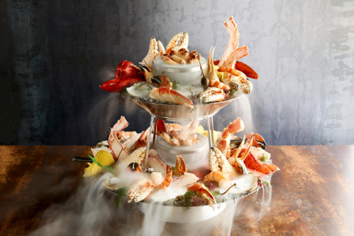 A three-tier seafood tower featuring shrimp, crab, and lobster, with smoke for a dramatic effect.