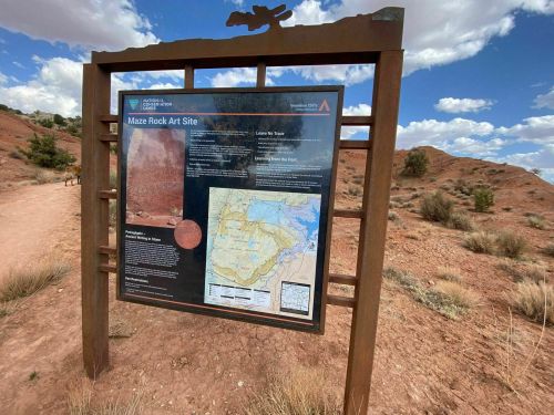 Sign for the Maze Rock Art Site, featuring information and a map, set against a desert landscape with blue skies.