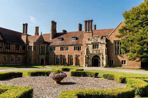 Historic brick building with ornate architecture, surrounded by manicured gardens and a central flowerbed.