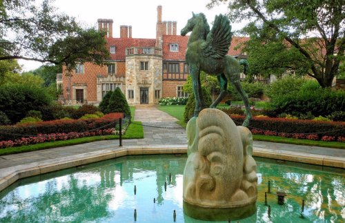 A bronze winged horse statue stands in a fountain, with a historic mansion and lush gardens in the background.