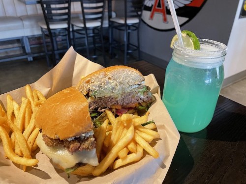A plate with two burgers and fries, alongside a blue drink with a lime slice in a jar.