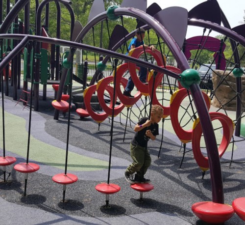 A child plays on a colorful playground structure with circular elements and climbing features on a sunny day.