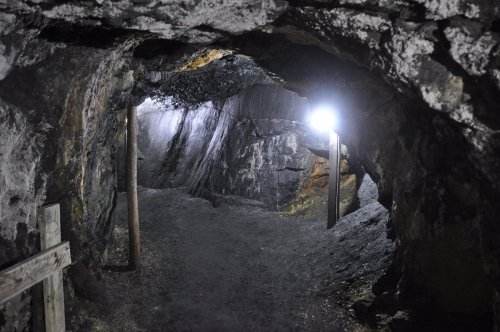 A dimly lit cave interior with rocky walls and a wooden support beam, illuminated by a bright light.