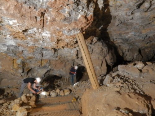 Two miners working in a rocky underground cave, with wooden supports and scattered stones around them.