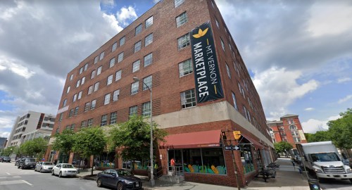 A brick building with a large sign reading "Mason Market Place" and trees lining the street in a city setting.