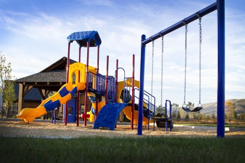 Colorful playground with slides and swings, set against a clear sky and grassy area.