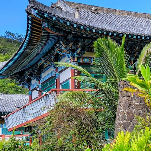A colorful traditional building with ornate architecture, surrounded by lush greenery and palm trees.