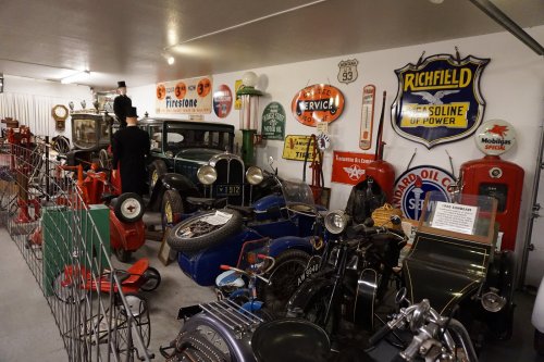 A vintage garage filled with classic cars, gas pumps, and retro signs, showcasing automotive history and memorabilia.