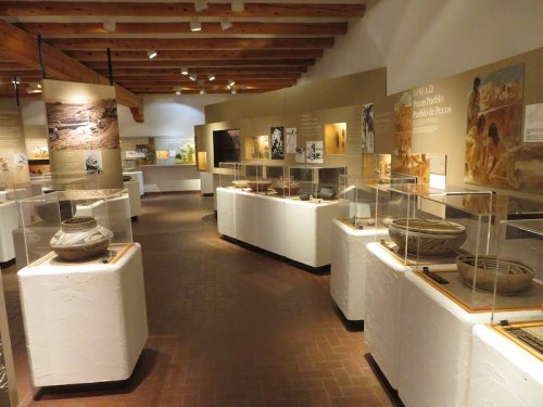 Interior of a museum exhibit featuring pottery and artifacts displayed in glass cases, with informative panels on the walls.