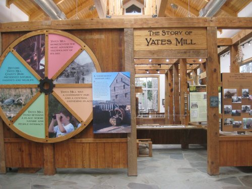 Interior view of Yates Mill exhibit, featuring a large informational wheel and displays about the mill's history.