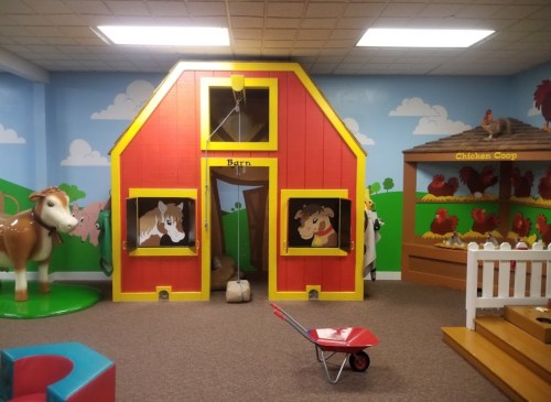 Colorful children's playroom featuring a barn, animal cutouts, and a wheelbarrow, with a farm-themed decor.