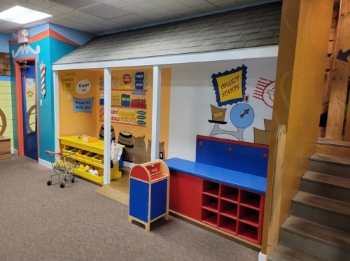 Colorful playroom with a storefront setup, featuring shelves, a mailbox, and playful wall decorations.