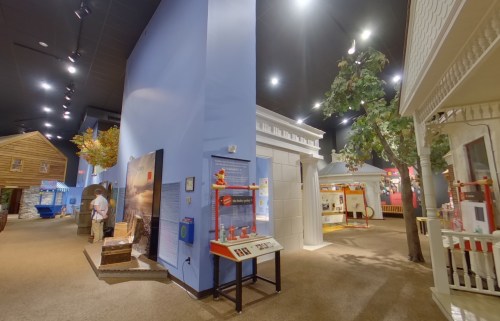 Interior view of a museum exhibit featuring various themed structures and displays under bright lights.