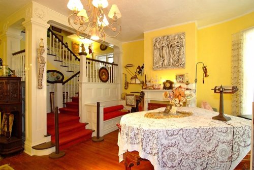 A cozy dining area with a lace tablecloth, yellow walls, and a staircase adorned with decorative items.