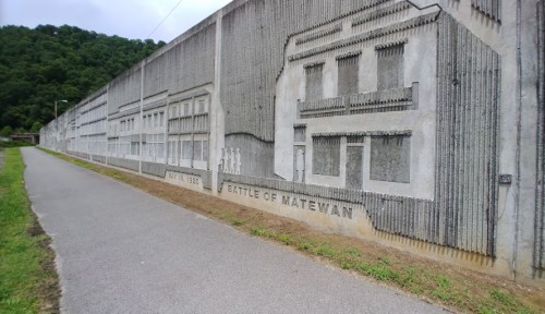 A concrete wall mural depicting buildings and the text "Battle of Matewan, July 1, 1920," alongside a walking path.