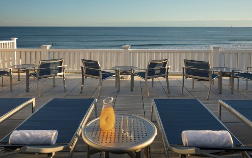 Lounge chairs by the ocean with a table holding a drink, overlooking calm waters and a clear sky.